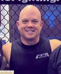 Brian Simril smiling in a black Freestyle Fighting Academy shirt in front of the cage
