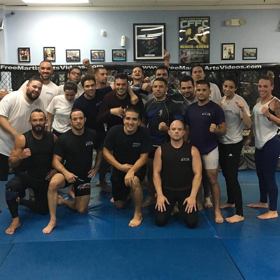 Estudiantes del programa Combat Athlete de pie juntos frente a la jaula en Freestyle Fighting Academy