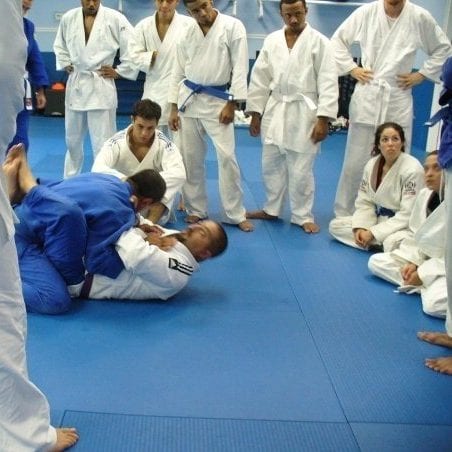 Estudiantes de Jiu-Jitsu brasileño con kimonos blancos y azules observando a dos compañeros luchar en el tatami en Freestyle Fighting Academy