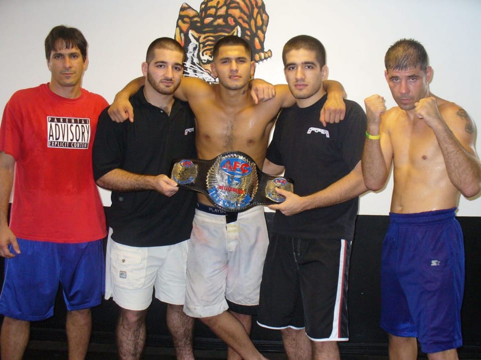 Un grupo de estudiantes adultos y entrenadores con guantes y vendas posando juntos después de una sesión de golpeo en Freestyle Fighting Academy en Miami