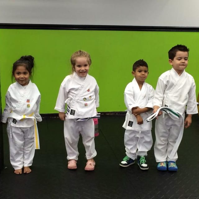 Cuatro niños pequeños con uniformes blancos de artes marciales y cinturones amarillos y blancos, juntos en la clase infantil de Freestyle Fighting Academy