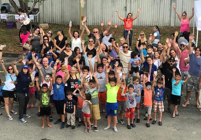 A large group of children and adults outside Freestyle Fighting Academy with their arms raised, cheering together after a class