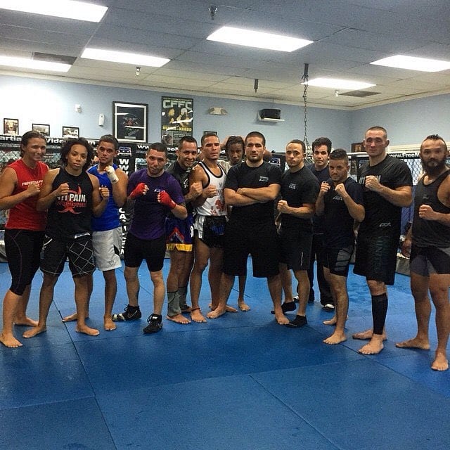 Members of the Freestyle Fighting Academy fight team standing together in training gear in front of the cage