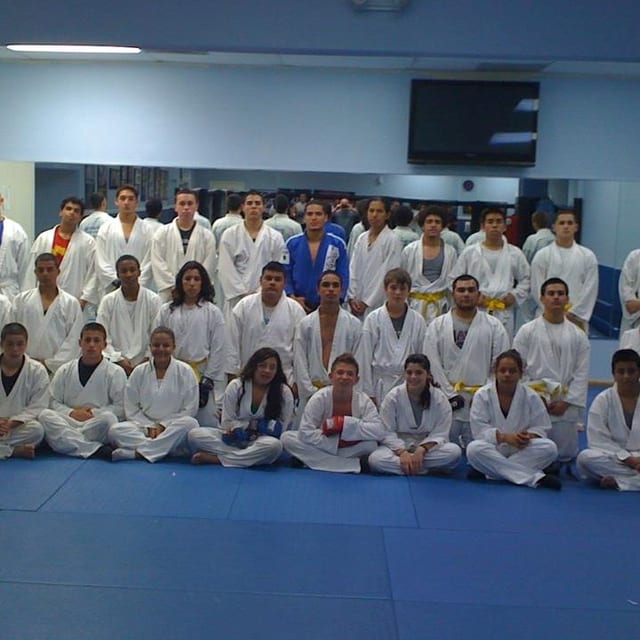 Un grupo grande de adolescentes con uniformes de artes marciales sentados juntos en el tatami de Freestyle Fighting Academy después de una clase
