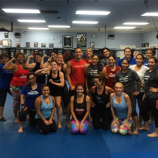 A large group of women in workout clothes posed together in the training room at the Women Only Fitness Bootcamp