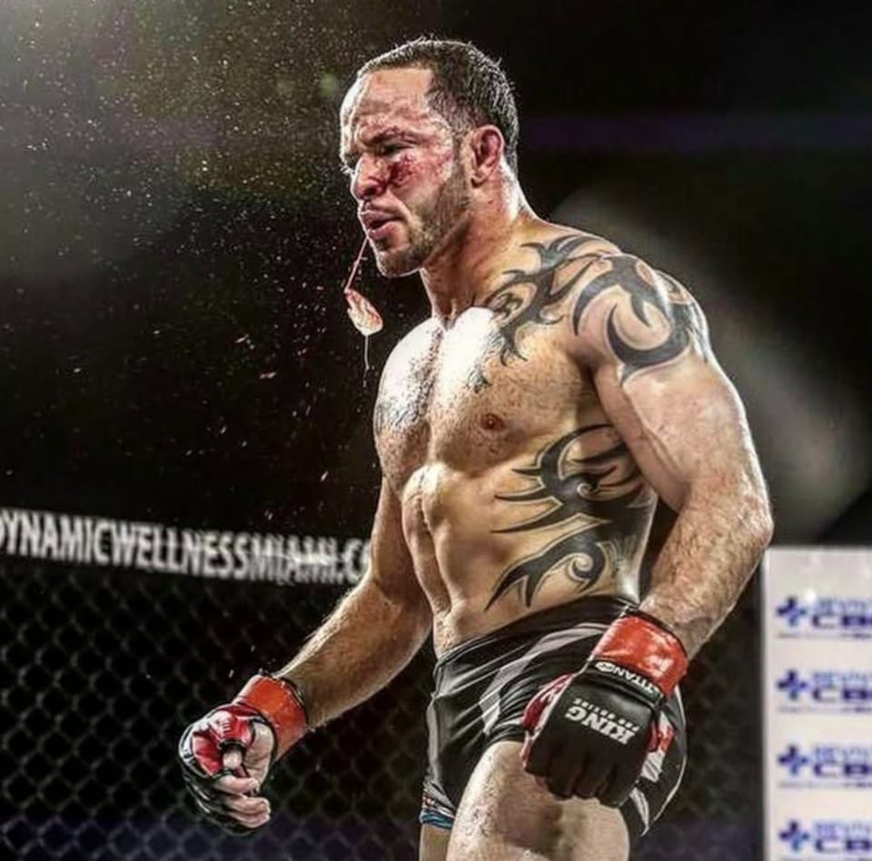 Jason Soares in the cage between rounds, bloodied and gloved, spitting water