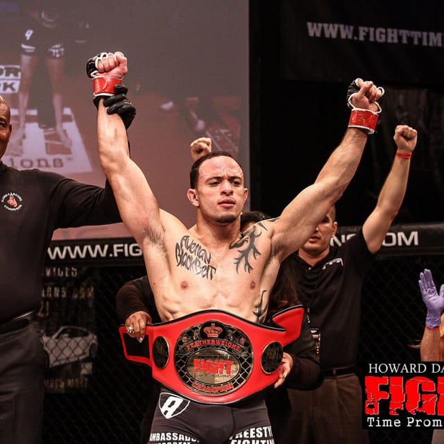 Jason Soares with his arms raised holding a championship belt in the cage after a Fight Time promotion bout