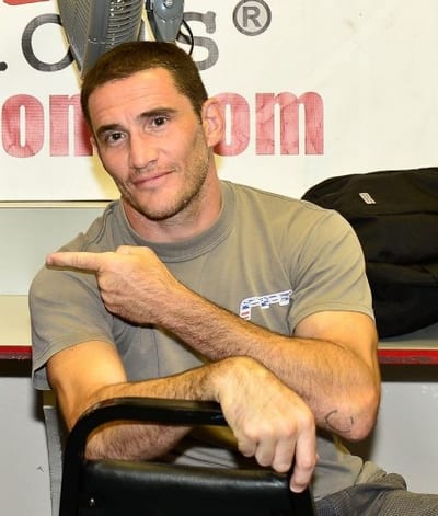 John Mangual seated in a grey T-shirt, pointing at the camera in front of the FFA banner