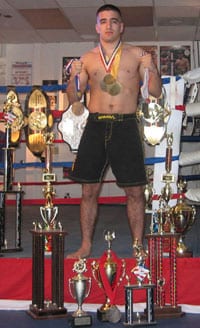 Marcos Avellan standing among championship trophies and title belts in the gym, wearing several medals around his neck