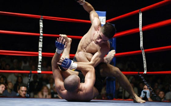 Marcos Avellan standing over a downed opponent in a boxing ring, throwing a punch from the top